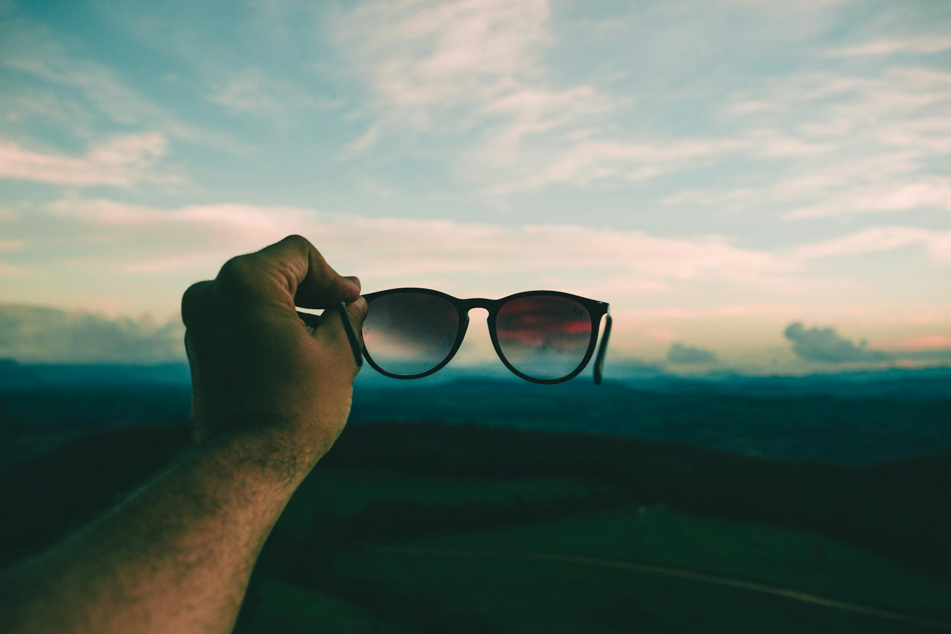 person holding black framed sunglasses under blue sky and white clouds